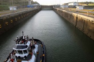 A tugboat navigates through a narrow canal with high concrete walls on either side. The canal appears to be part of the Panama Canal.