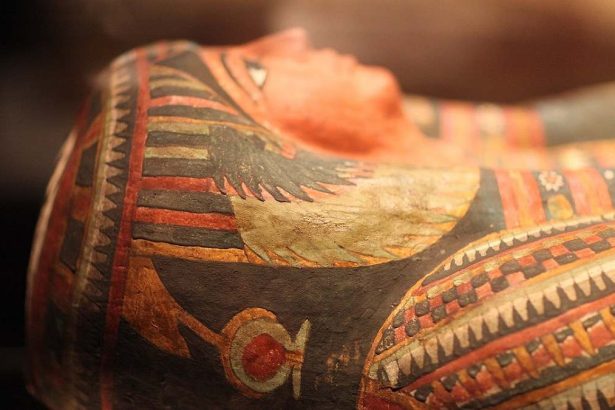 Close-up of an ancient Egyptian mummy's face, showing intricate painted designs and details.